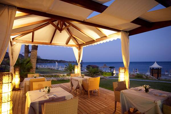 Außenbereich des Rodos Palladium Leisure & Wellness mit Tischen und Stühlen, beleuchtet und Blick auf das Meer.