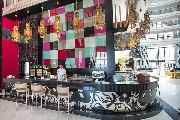 Innenansicht der Bar im Seaden Sea Planet Resort & Spa mit farbigen Wänden und Mustern, goldenen Kronleuchtern und einem Barkeeper, der hinter der Theke steht.