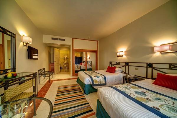 Hotelzimmer mit zwei Betten, Wandleuchten, Tisch, Fernseher, Spiegel und Einrichtungsgegenständen.
