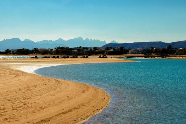 Eine Strandlandschaft mit blauem Wasser, sandigem Strand und Bergen im Hintergrund.