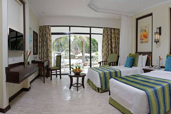 Zwei Doppelbetten in einem Hotelzimmer von Sarova Whitesands Beach Resort & Spa mit Blick auf eine Terrasse und einen Pool.