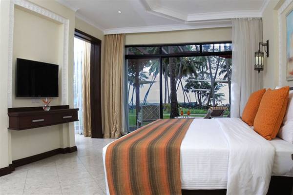 Innenansicht eines Zimmers im Sarova Whitesands Beach Resort mit Bett, Fernseher und Glasfenstern zum Meer