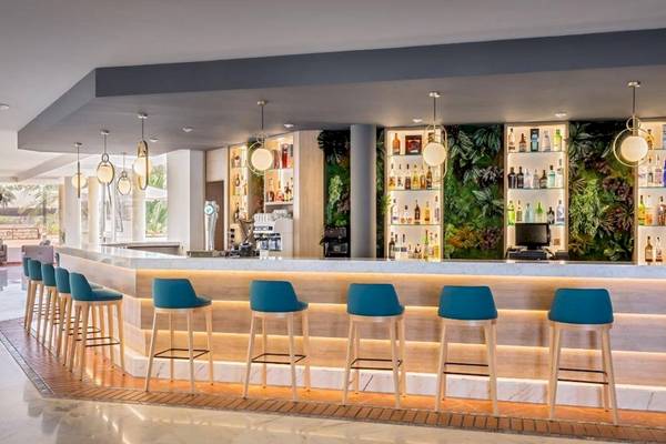 Bar im Barcelo Corralejo Bay Hotel mit grüner Wand, vielen Flaschen und blauen Stühlen