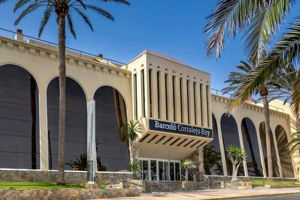 Außenansicht des Barcelo Corralejo Bay Hotels mit Palmen und bogenförmigen Fenstern.