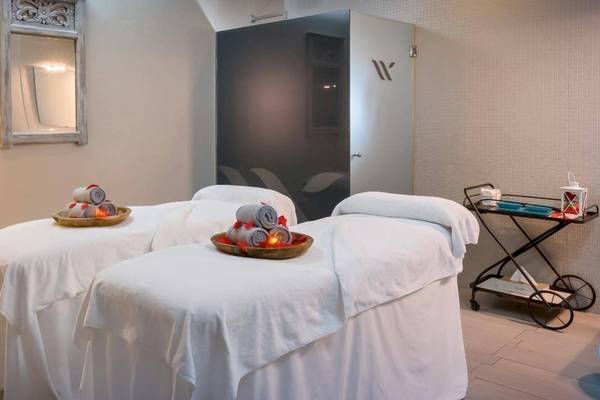 Massageraum im Barcelo Corralejo Bay Hotel mit zwei Massagetischen, Kissen und Kerzen.