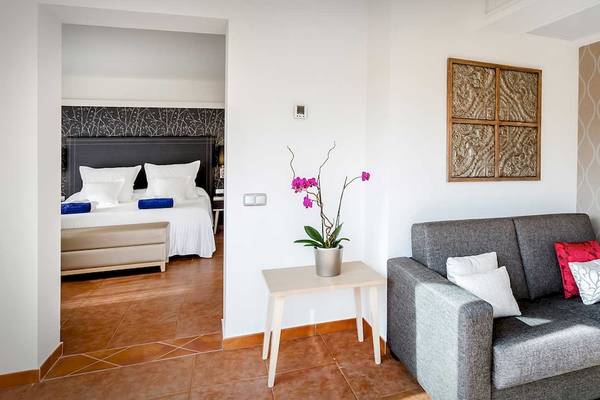 Innenansicht eines Zimmers im Barcelo Corralejo Bay Hotel mit Bett, Sofa, Tisch und Kunstwerk an der Wand.