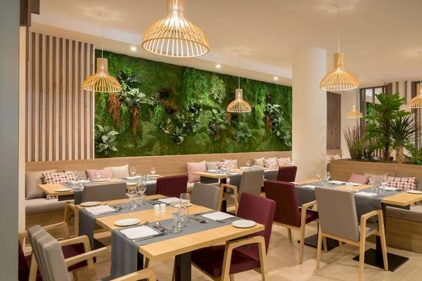Innenbereich des Restaurants des Barcelo Corralejo Bay Hotels mit grüner Wand, Holztischen und Stühlen.