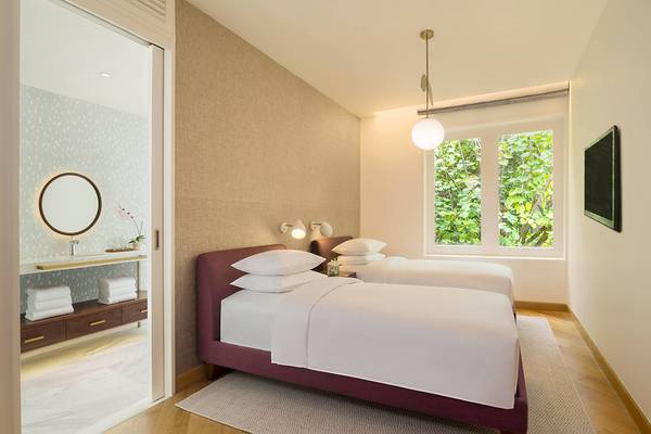 Schlafzimmer im JW Marriott Maldives Resort & Spa mit zwei Betten, weißem Bettwäsche, zwei Lampen und einem Fenster mit Ausblick auf Bäume.