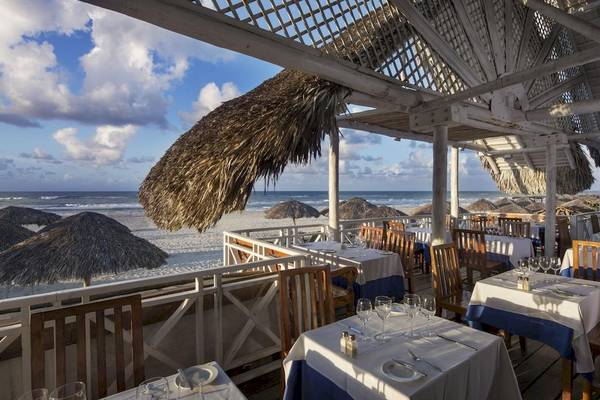 Außenterrasse des Royalton Hicacos Resort & Spa mit Tischen und Stühlen unter Strohdächern am Strand