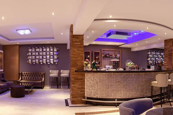 Innenansicht der Bar im Asterias Beach Hotel mit modernen Möbeln und violetten Akzenten.