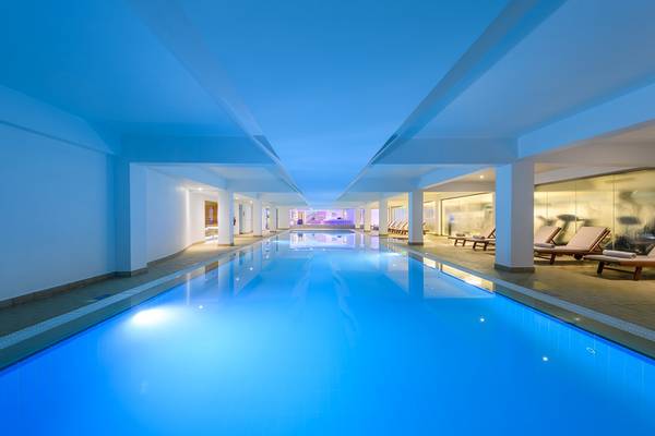 Innenpool des Asterias Beach Hotels mit blauen Wasser und weißen Säulen.