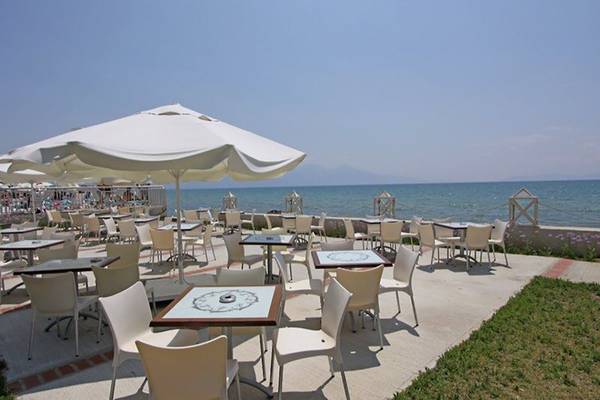 Terrasse des Ephesia Holiday Beach Club Hotels mit Tischen und Stühlen, Blick auf das Meer.
