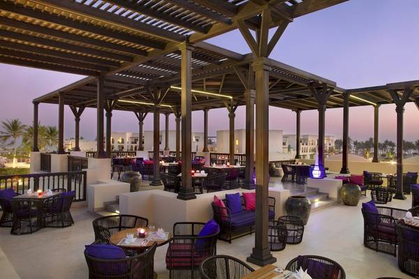 Abendansicht des Terrassenrestaurants im Salalah Rotana Resort mit beleuchteten Tischen und Stühlen.