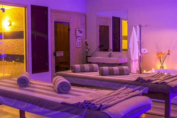 Behandlungsraum im Serenity Alma Heights Spa mit zwei Massageliegen, violetten Lichtern und einem Waschbecken.