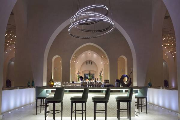 Innenansicht der Bar im Salalah Rotana Resort mit Theke, Stühlen und Beleuchtung.