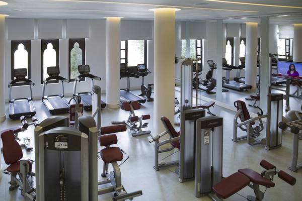 Fitnessstudio im Salalah Rotana Resort mit diversen Geräten und einer Frau auf dem Fernsehbildschirm.