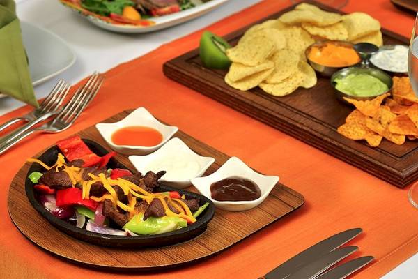 Ein Tisch mit verschiedenen Gerichten und Chips auf einem orangefarbenen Tischtuch.