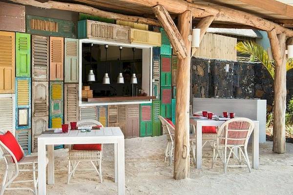 Außenbereich des Zilwa Attitude Hotels mit bunten Fensterläden und Tischen und Stühlen auf weißem Sand.