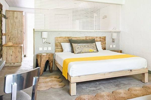 Ein modernes Hotelzimmer im Zilwa Attitude mit weißem Bett, gelber Decke, Holzbettrahmen, Nachttischen und Wanddekoration.