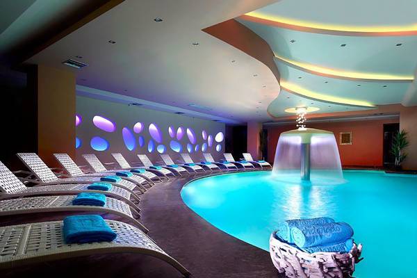 Innenpool des Michelangelo Resort & Spa mit blau beleuchteten Wänden und Liegen.