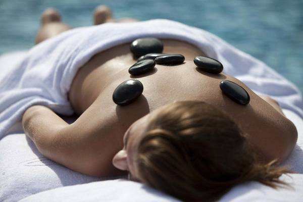 Frau mit Steinen auf dem Rücken im Wasser liegend, wohltuende Massage genießend.
