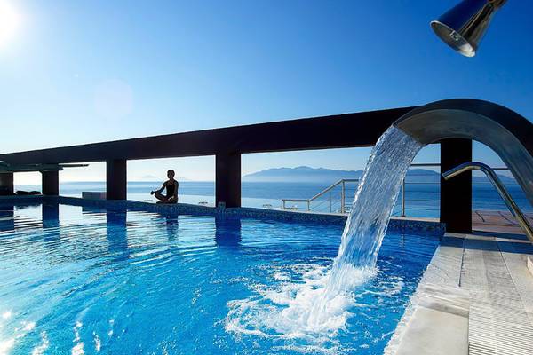 Außenpool des Michelangelo Resort & Spa mit Blick auf das Meer und eine Frau in Meditationshaltung.
