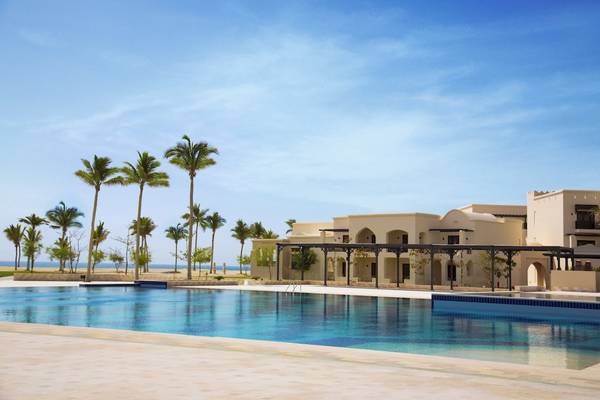 Außenpool des Salalah Rotana Resorts mit weißen Gebäuden im Hintergrund und Palmen