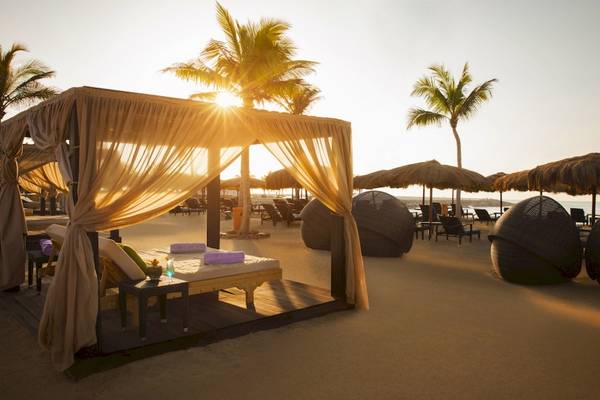 Strandzeltbett im Salalah Rotana Resort mit Sonnenaufgang und Palmen im Hintergrund.