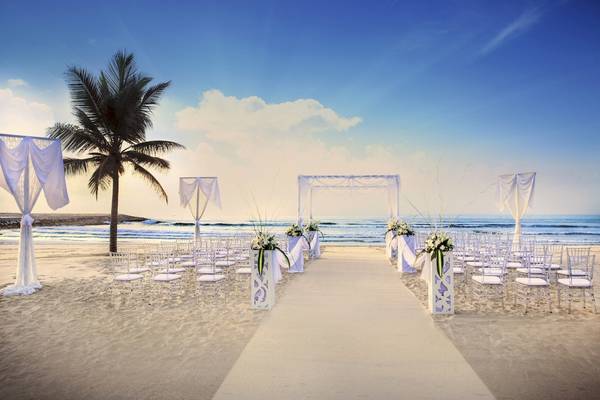 Hochzeitszeremonie am Strand im Salalah Rotana Resort mit weißen Stühlen und Blumenarrangements.