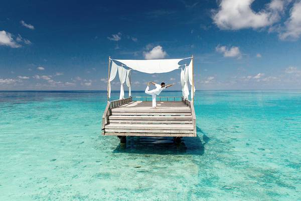 Eine Person praktiziert Yoga auf einer Plattform im Wasser am Baros Maldives Resort.