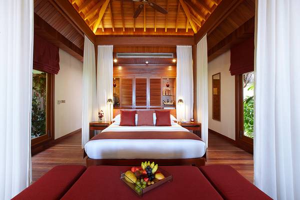 Schlafzimmer im Baros Maldives Resort mit einem großen Bett, roten Kissen und einer Obstplatte auf einem Tisch.