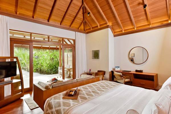 Innenansicht eines Zimmers im Baros Maldives Resort mit einem großen Bett, einem Schreibtisch und einer Terrasse.