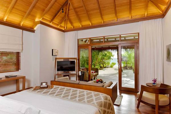 Schlafzimmer im Baros Maldives Resort mit großem Bett und Aussicht auf den Strand.