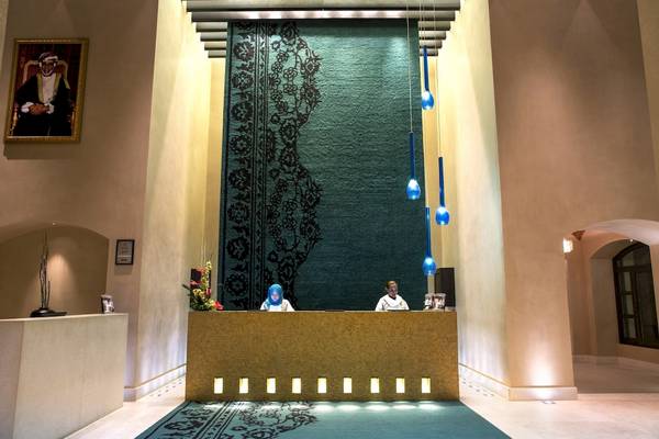 Empfangsbereich des Salalah Rotana Resorts mit zwei Mitarbeitern am Empfang und einer Wanddekoration.