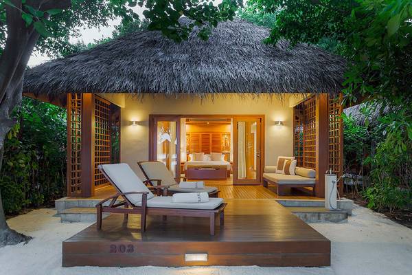 Außenbereich der Baros Maldives Resort Hütte mit Liegestühlen und einem Bett