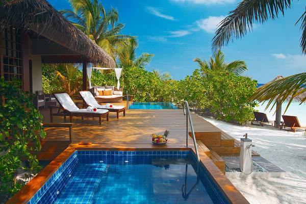 Ein Pool auf der Terrasse im Baros Maldives Resort mit Lounge-Liegen und Palmen.