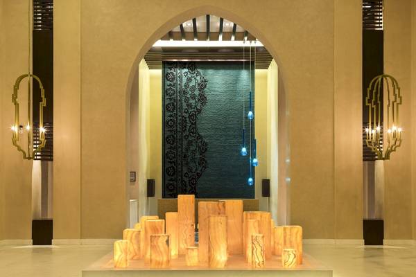 Der Eingangsbereich des Salalah Rotana Resorts mit einem großen Bogen, Wandleuchten und einem Wandteppich.