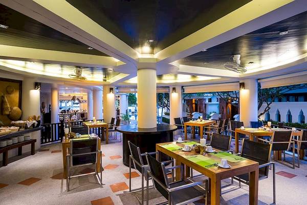 Innenansicht des Restaurants im Dara Samui Beach Resort mit runden und rechteckigen Tischen und Stühlen, hohen Decken und offenen Fenstern.