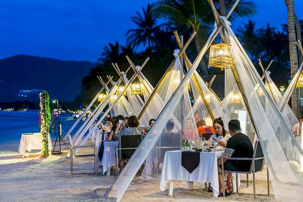 Beleuchtete Zelte mit Tischen und Stühlen auf dem Strand des Dara Samui Beach Resorts.