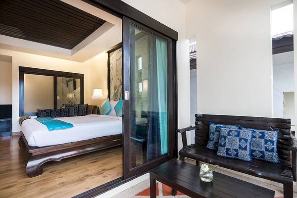 Innenansicht eines Zimmers im Dara Samui Beach Resort mit einem Bett, einer Bank und einem Tisch.