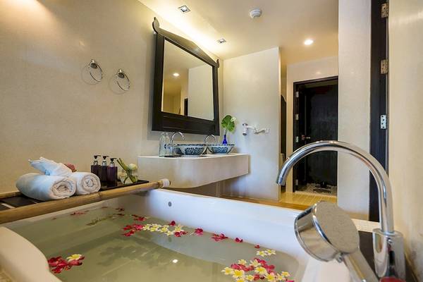Badezimmer im Dara Samui Beach Resort mit Badewanne, Blumen, Spiegel und Waschbecken.