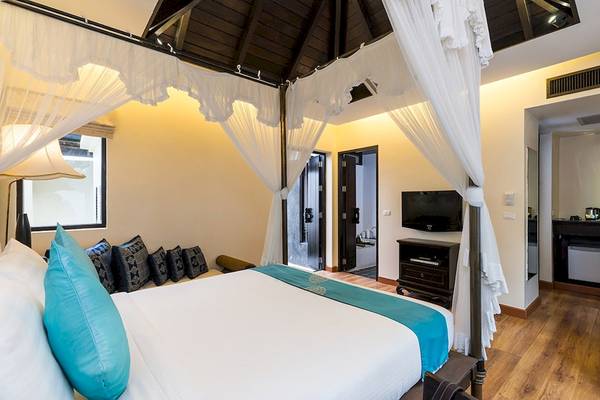Ein Bettzimmer im Dara Samui Beach Resort mit einem Himmelbett, blauen Kissen und einem Fernseher.