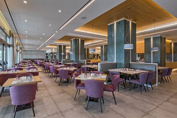 Restaurant des Amada Colossos Resorts mit vielen Tischen und Stühlen, hoher Decke und Marmorsäulen.