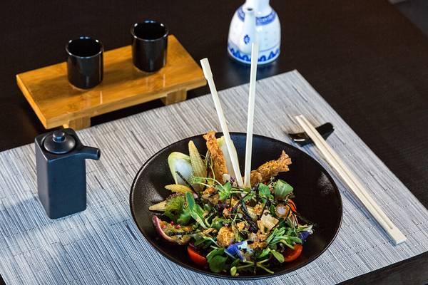 Ein Salat in einem schwarzen Teller mit Besteck auf dem Tisch, umgeben von Utensilien.
