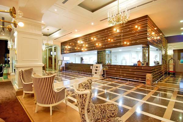 Lobby des Delphin Diva Premiere Hotels mit gemustertem Boden, Empfangstresen und goldenen Kronleuchtern.