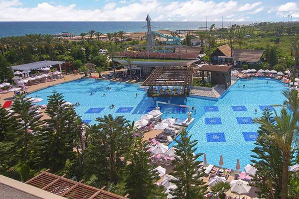 Luftaufnahme des Delphin Diva Premiere Pools mit Wasserrutsche, Sonnenschirmen und Hotel im Hintergrund.