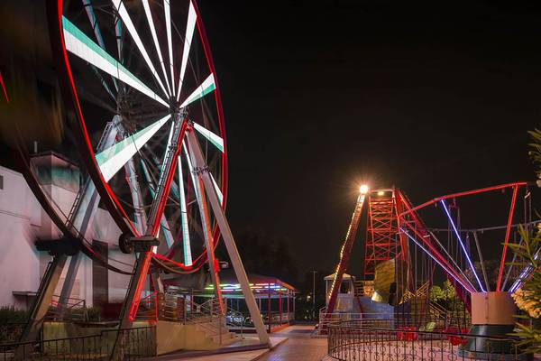 Nachtaufnahme des Delphin Diva Premiere Hotels mit Achterbahn und Riesenrad im Vordergrund.