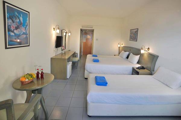 Zimmer im Nissiana Hotel mit drei Betten, Tisch, Stuhl, Dekor und Fernseher.