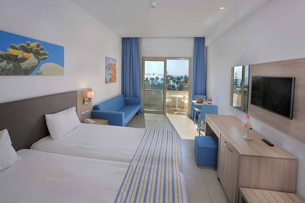 Innenansicht eines Hotelzimmers im Nissiana Hotel mit zwei Betten, einem Sofa und einem Ausblick auf das Meer.