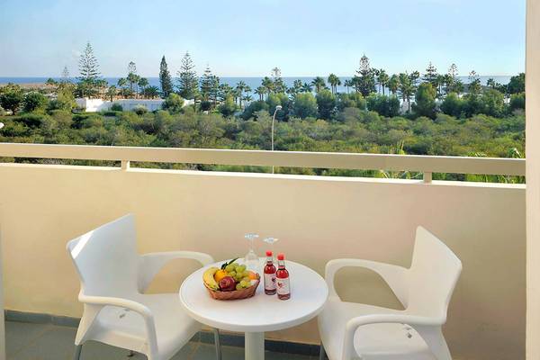 Balkon mit Meerblick im Nissiana Hotel mit zwei weißen Stühlen, einem Tisch mit Früchten und Getränken.